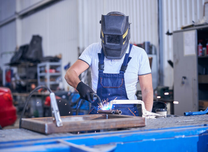 Mechanic wearing work overalls and protective face mask while using welding torch at auto service station